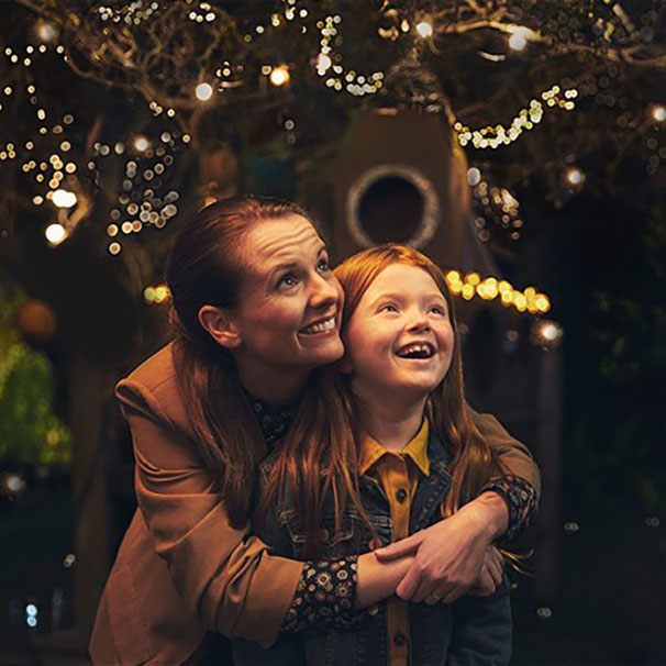 Mother embraces her daughter while enjoying the mesmerizing glow of Christmas lights.
